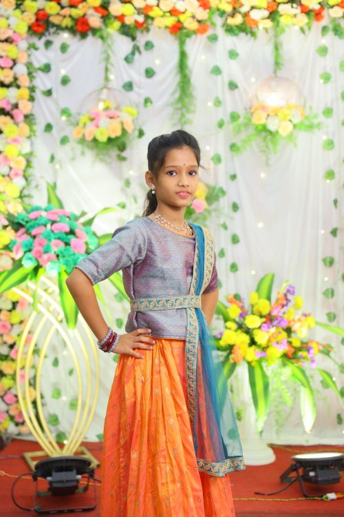 Free A young girl poses elegantly in colorful traditional Indian attire with a floral backdrop. Stock Photo