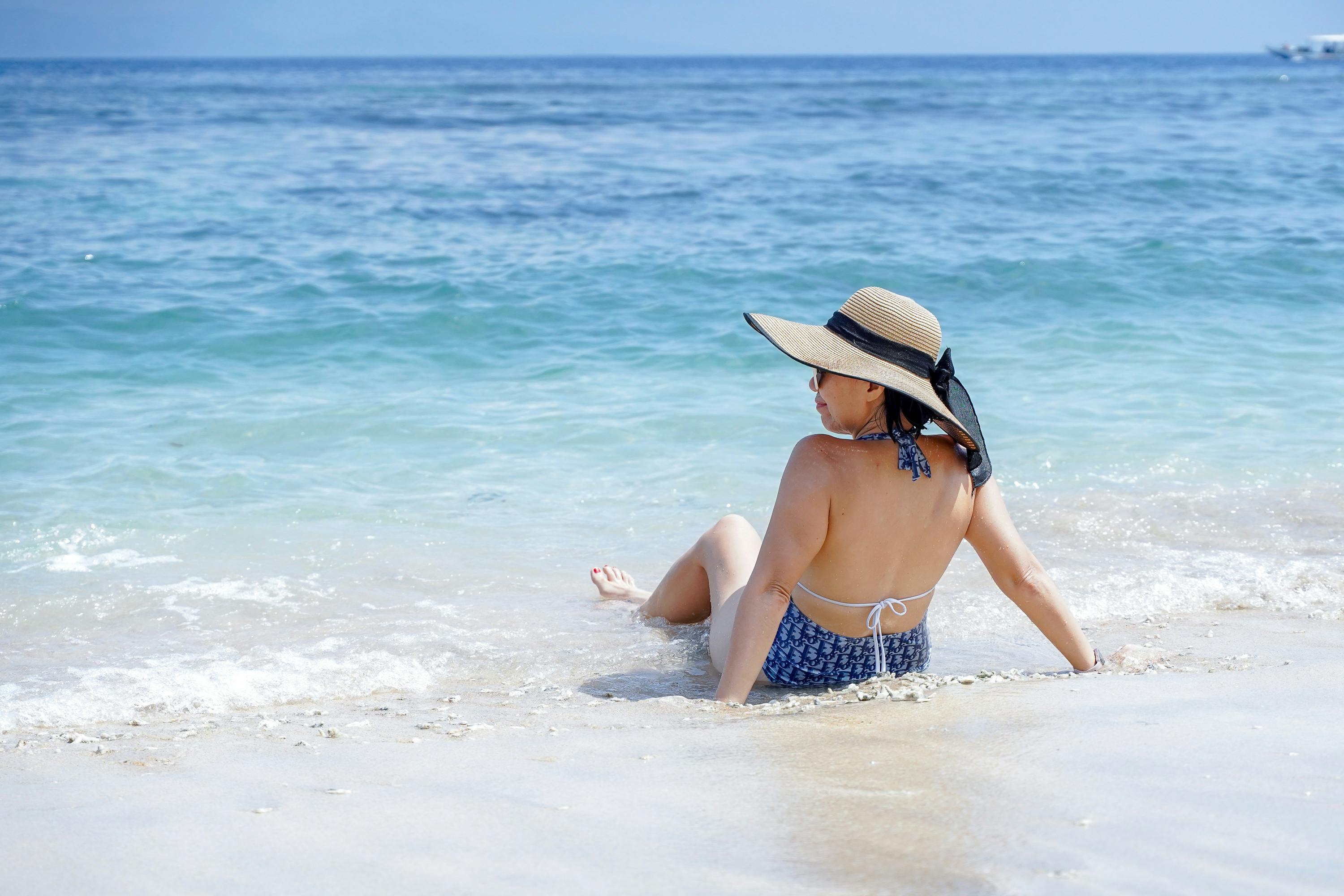 A woman relaxes on a sandy beach, enjoying the sunny summer day beside the ocean. - Photo by Agus Jaya on Pexels