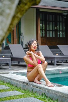 Asian woman in swimsuit by the poolside enjoying a sunny day outdoors.