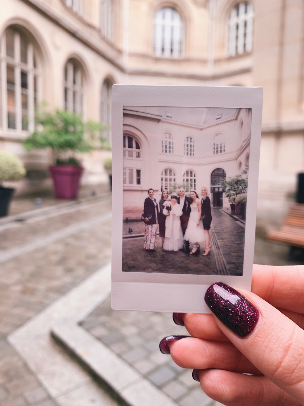 A Polaroid photo capturing a Parisian wedding in a classic courtyard setting held by a hand with painted nails.