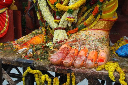 Close-up of statue feet covered in flowers and garlands, showcasing vibrant colors and cultural details.