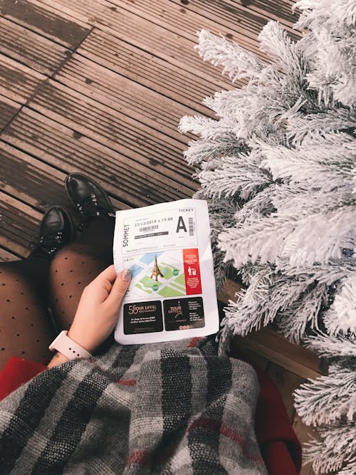 Woman Holding a Ticket While Sitting Next to a Christmas Tree