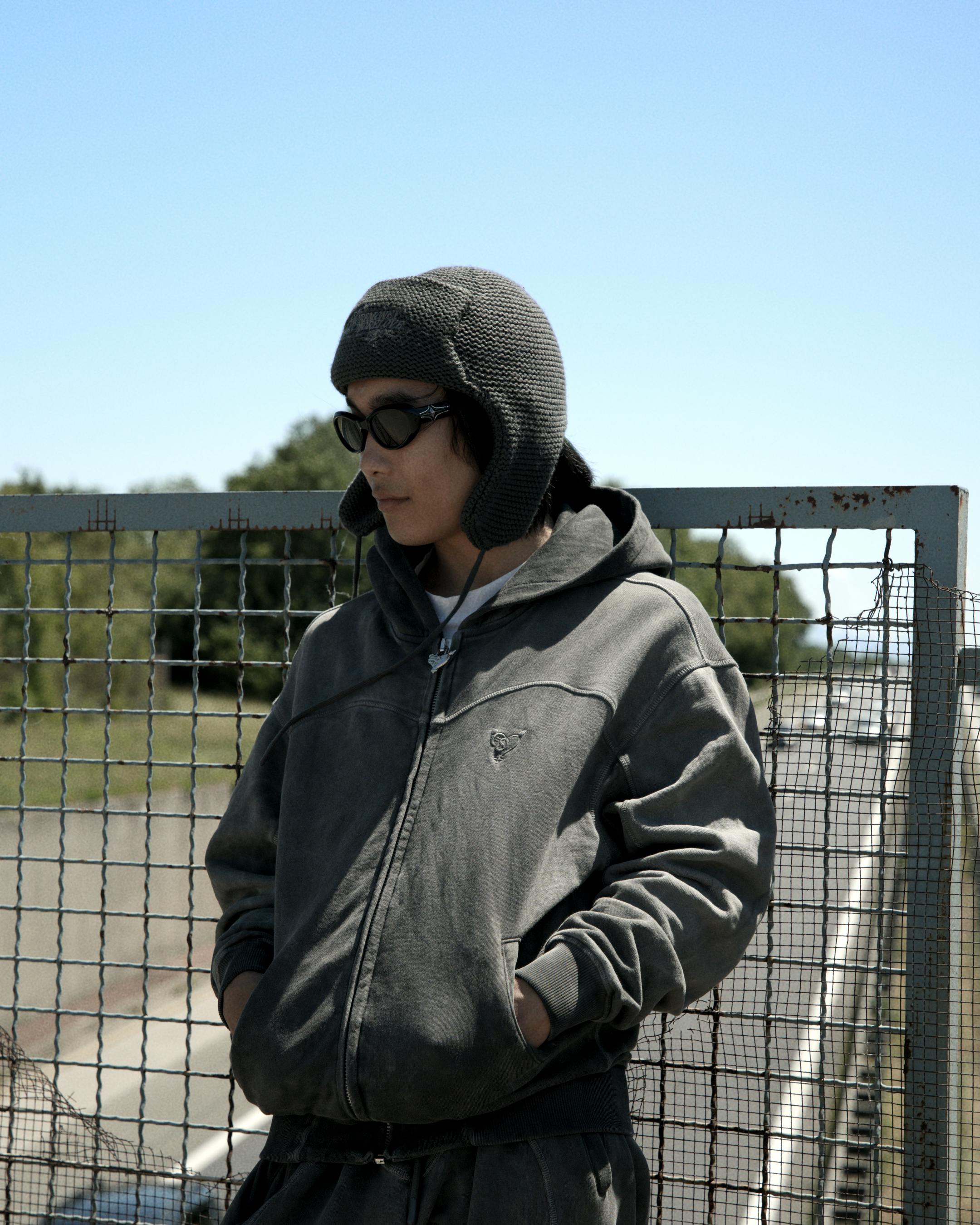Free Person in cozy streetwear posing on an urban overpass, showcasing casual fashion style. Stock Photo