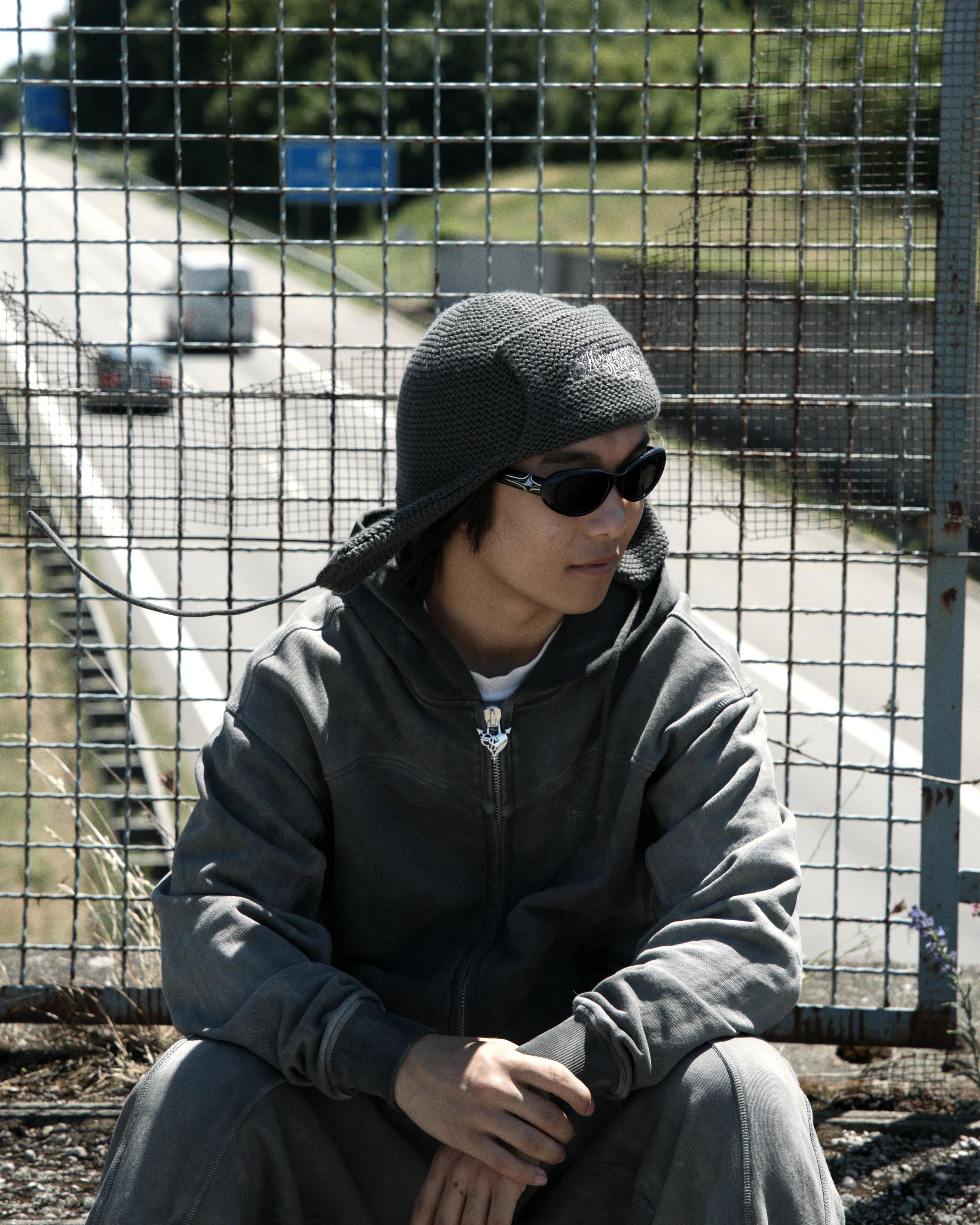 Free Man in casual clothing sitting near a highway fence on a bright day. Stock Photo