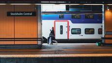 Woman walking with luggage at Stockholm Central Station's platform, beside a train.