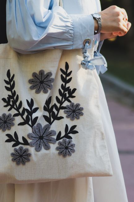 Close-up of a tote bag featuring elegant black floral embroidery, held by a person outdoors. - best handbag for different occasions