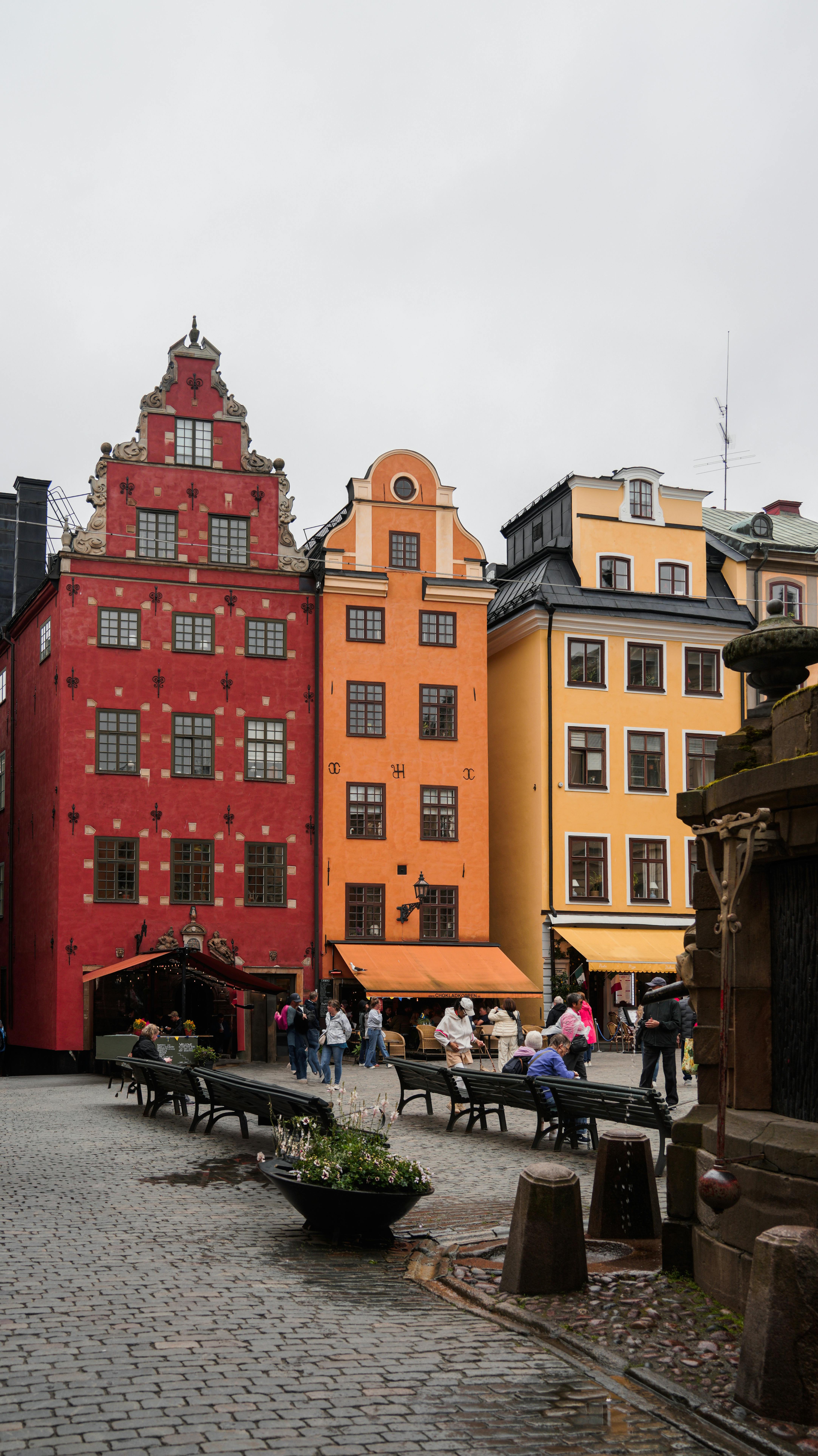Vibrant facades in Stockholm's Gamla Stan with people in the square below on a cloudy day.