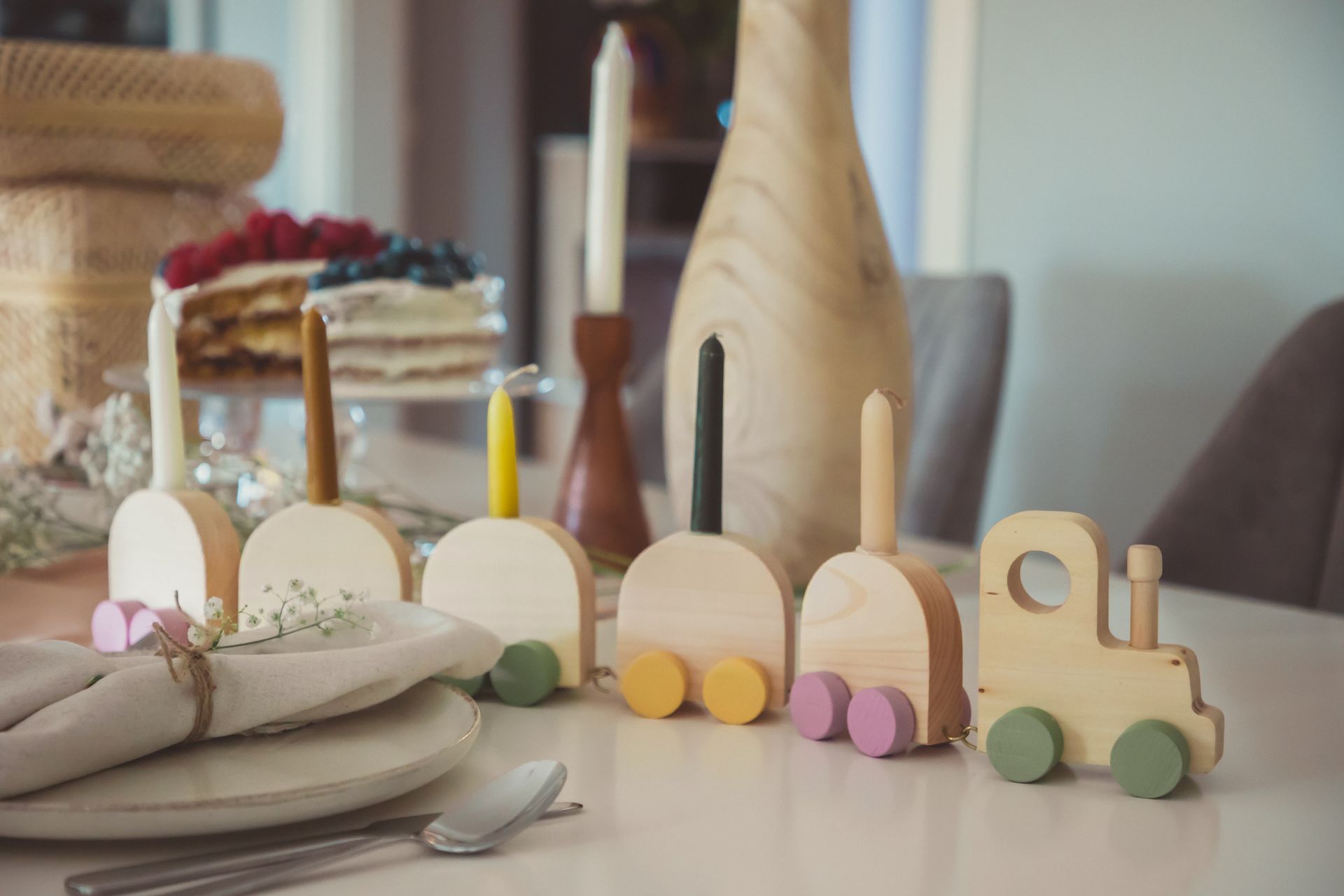 Wooden toy train and elegant table setting with cake, candles, and decorations.