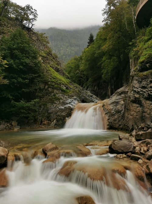 Free A beautiful waterfall flowing through a rocky forest landscape under a misty sky. Stock Photo