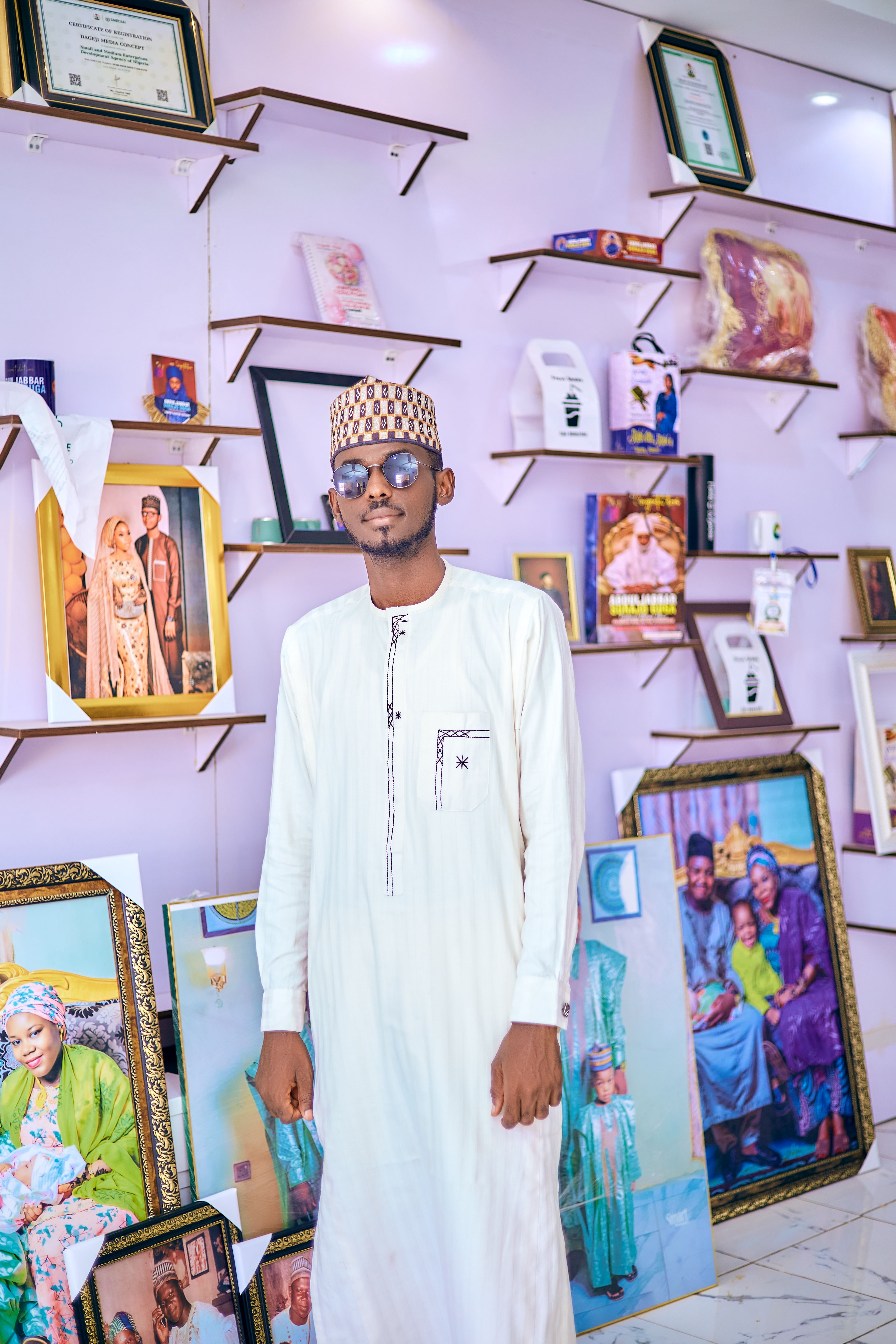 Man in traditional attire stands in art gallery with framed photos on walls.