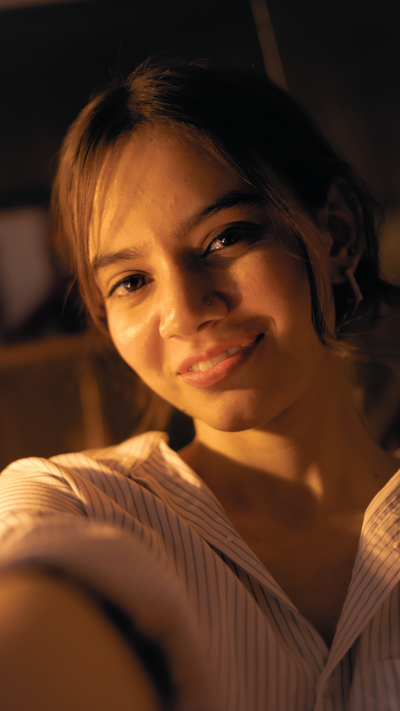 A young woman taking a cozy selfie indoors with warm lighting and a relaxed expression.