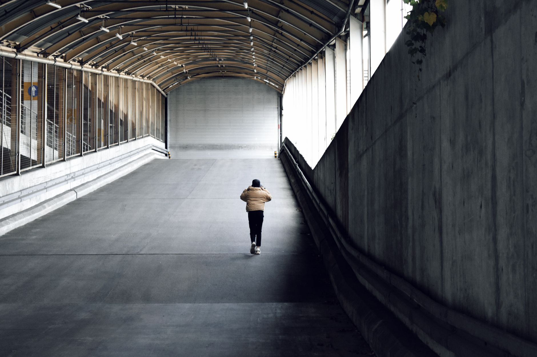 A lone person walks up a covered urban tunnel, showcasing solitude and urban architecture.