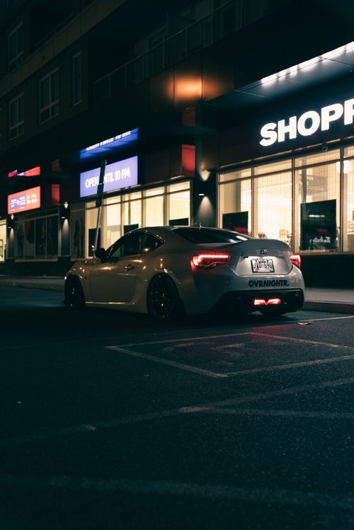 Free White sports car parked under neon city lights at night, showcasing urban lifestyle. Stock Photo