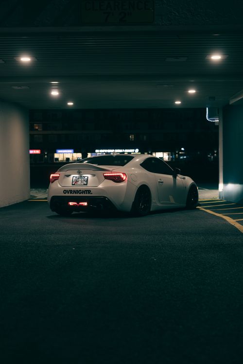Free White sports car parked in an urban garage at night. Modern, sleek design with subtle lighting. Stock Photo