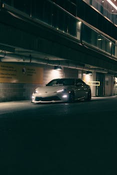Stylish sports car parked in a moody, dimly lit urban parking garage at night.