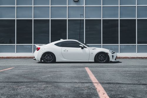 Free A white sports car parked in an empty lot in front of a large glass building facade. Stock Photo