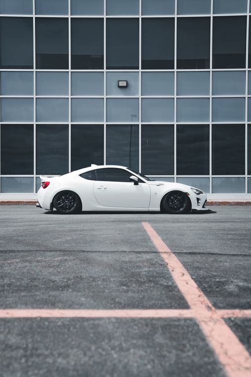 Free Side view of a stylish white sports car parked against a grid-patterned building facade. Stock Photo
