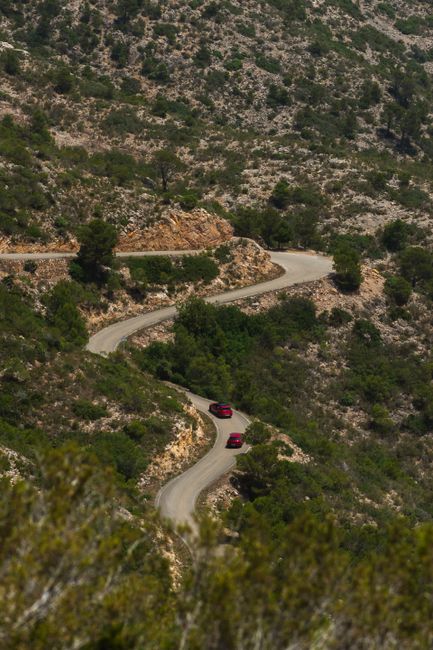Aerial view of red cars on a winding mountain road surrounded by rugged terrain.