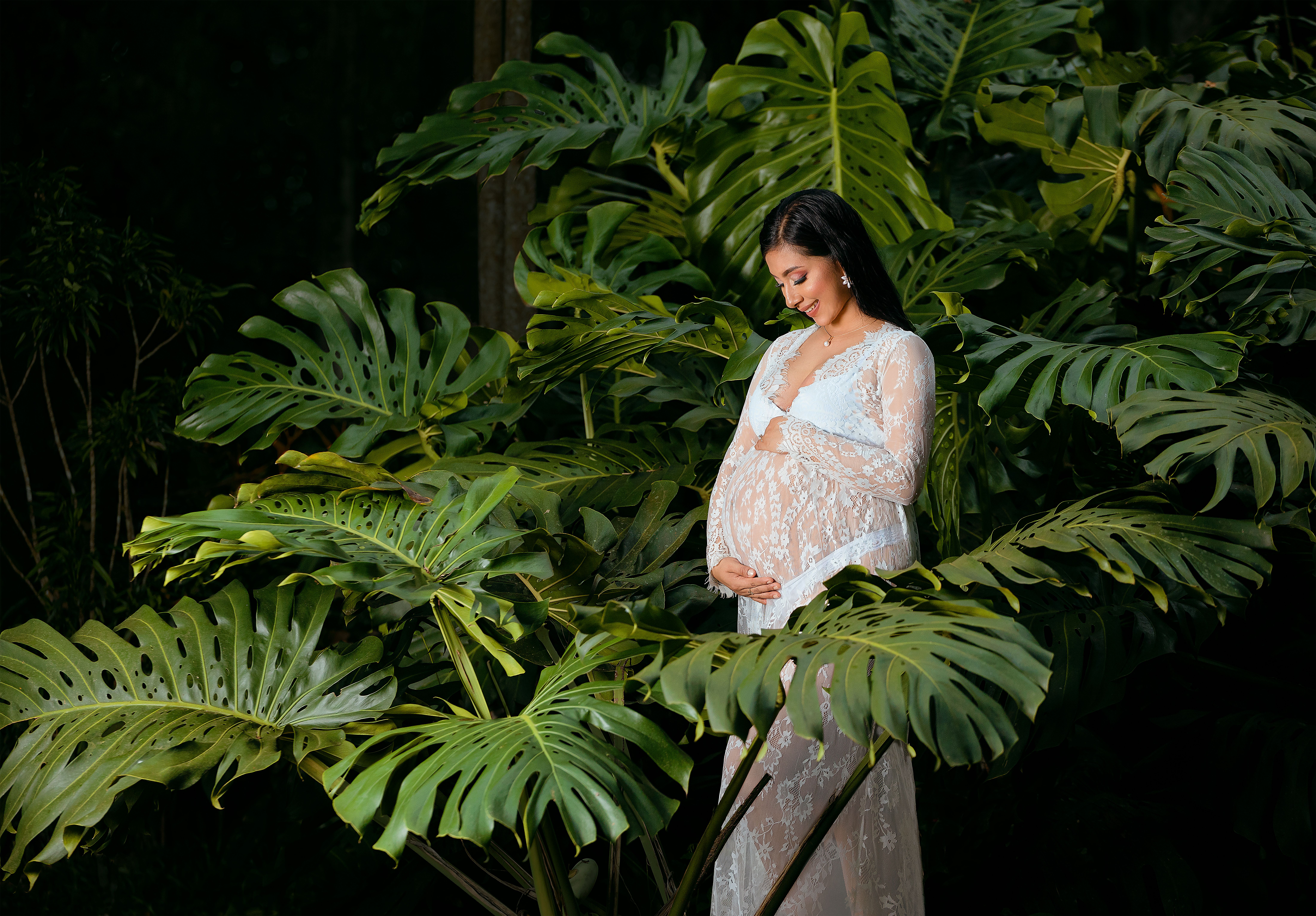 A serene portrait of a pregnant woman surrounded by lush tropical foliage.