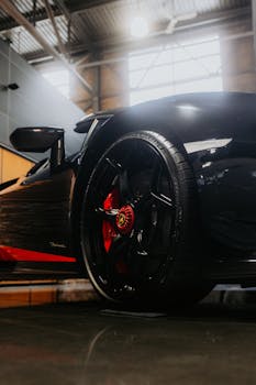 Detailed view of a luxury sports car wheel in an industrial garage setting, highlighting design and elegance.
