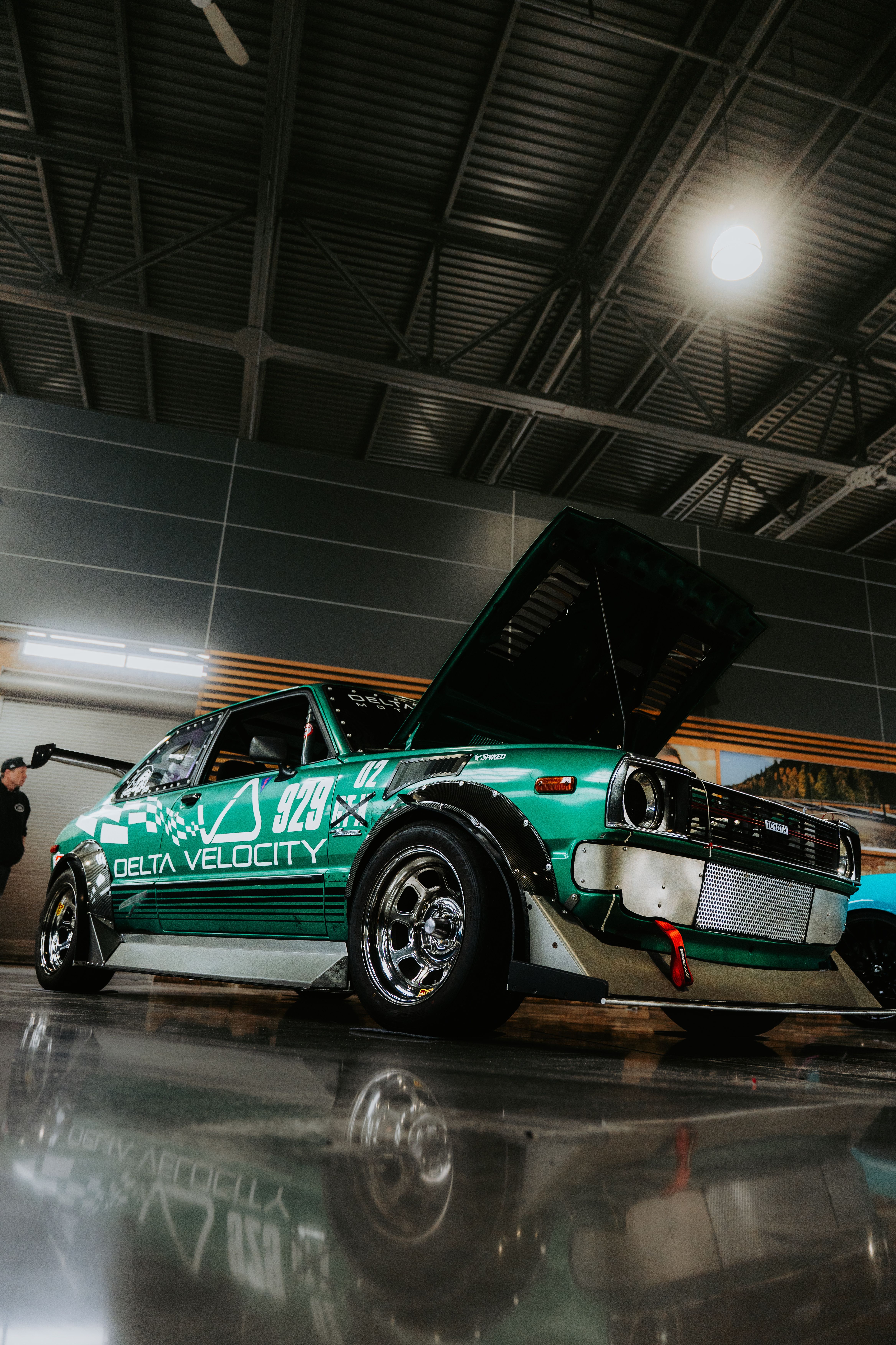 A vintage green race car with an open hood showcased indoors, showcasing automotive detailing.