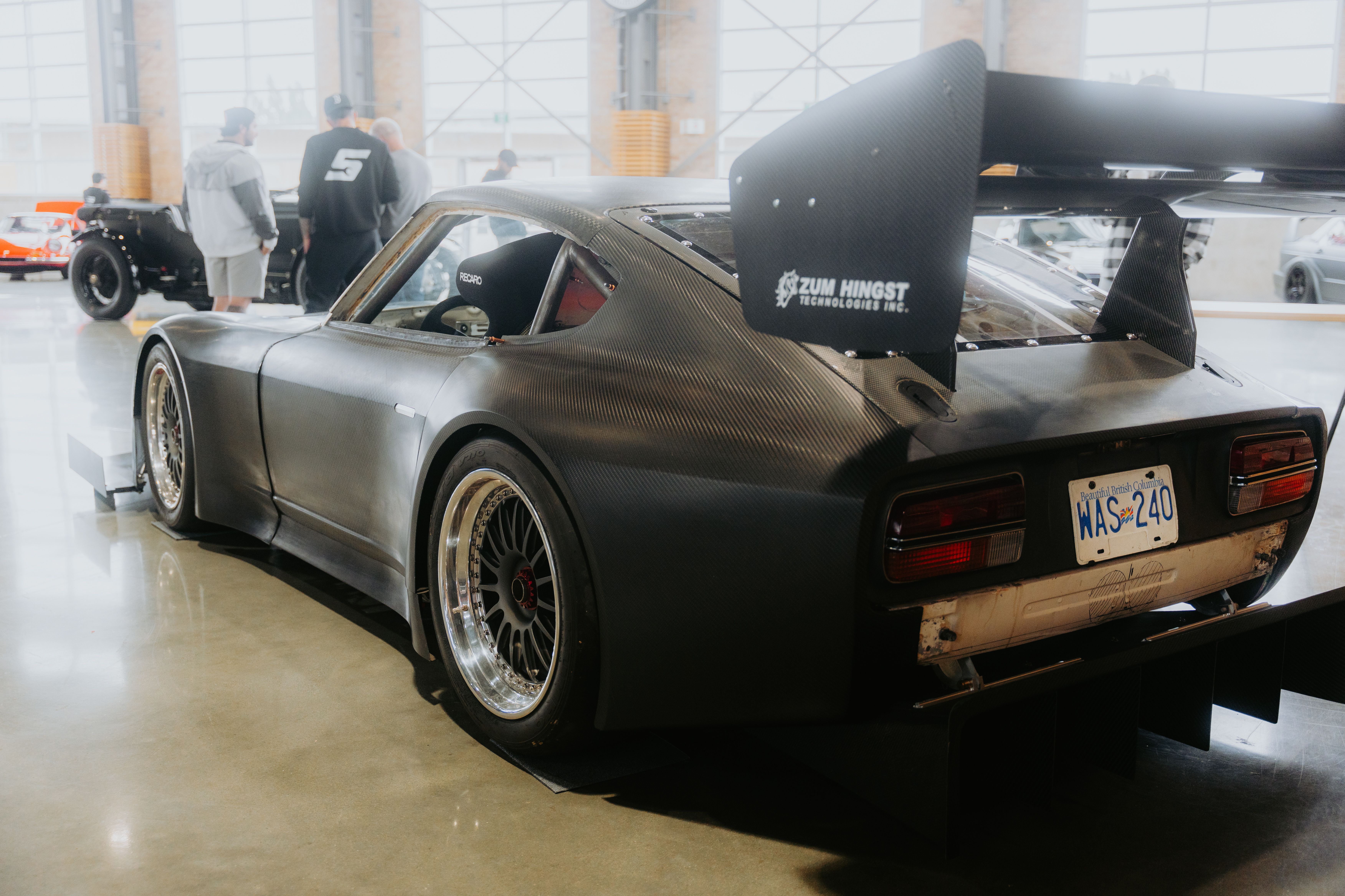 High-performance sports car with rear spoiler at an indoor auto show. Attendees in background.
