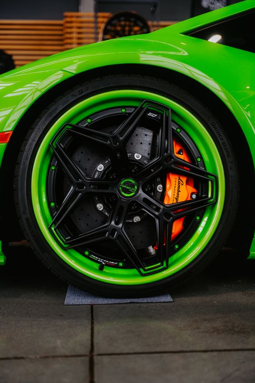 Free Detailed shot of a green sports car wheel highlighting sleek black rim and orange brake caliper. Stock Photo