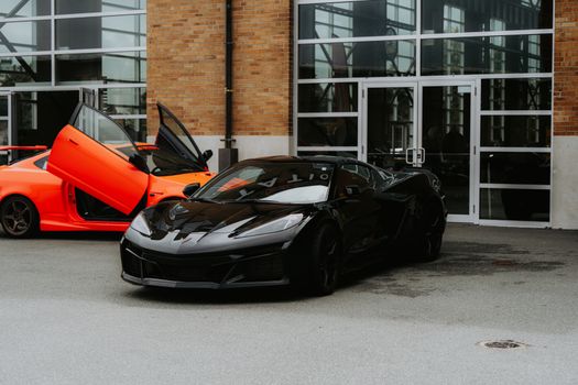 Black and orange luxury sports cars parked outside an industrial-style building.
