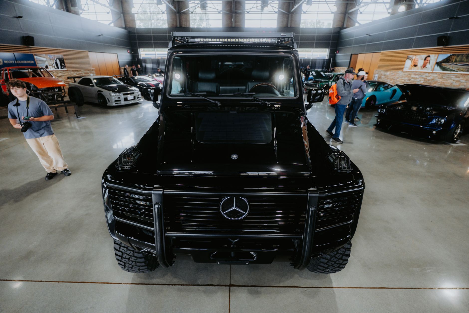 Front view of a black luxury SUV displayed at an indoor auto show with other vehicles.