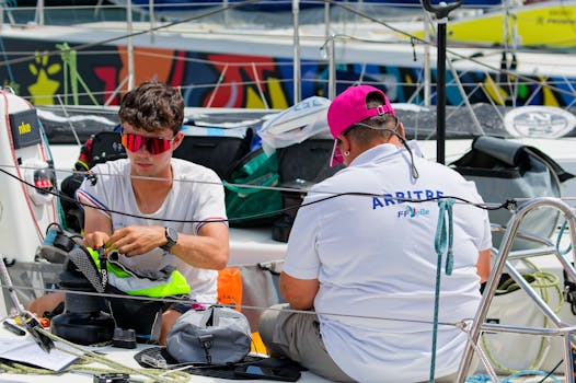 Crew members prepare equipment on a sailboat during a sunny day at the marina.