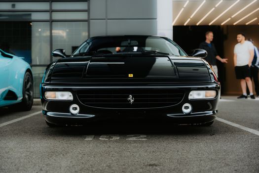 Front view of a classic black sports car parked outdoors with people chatting nearby.