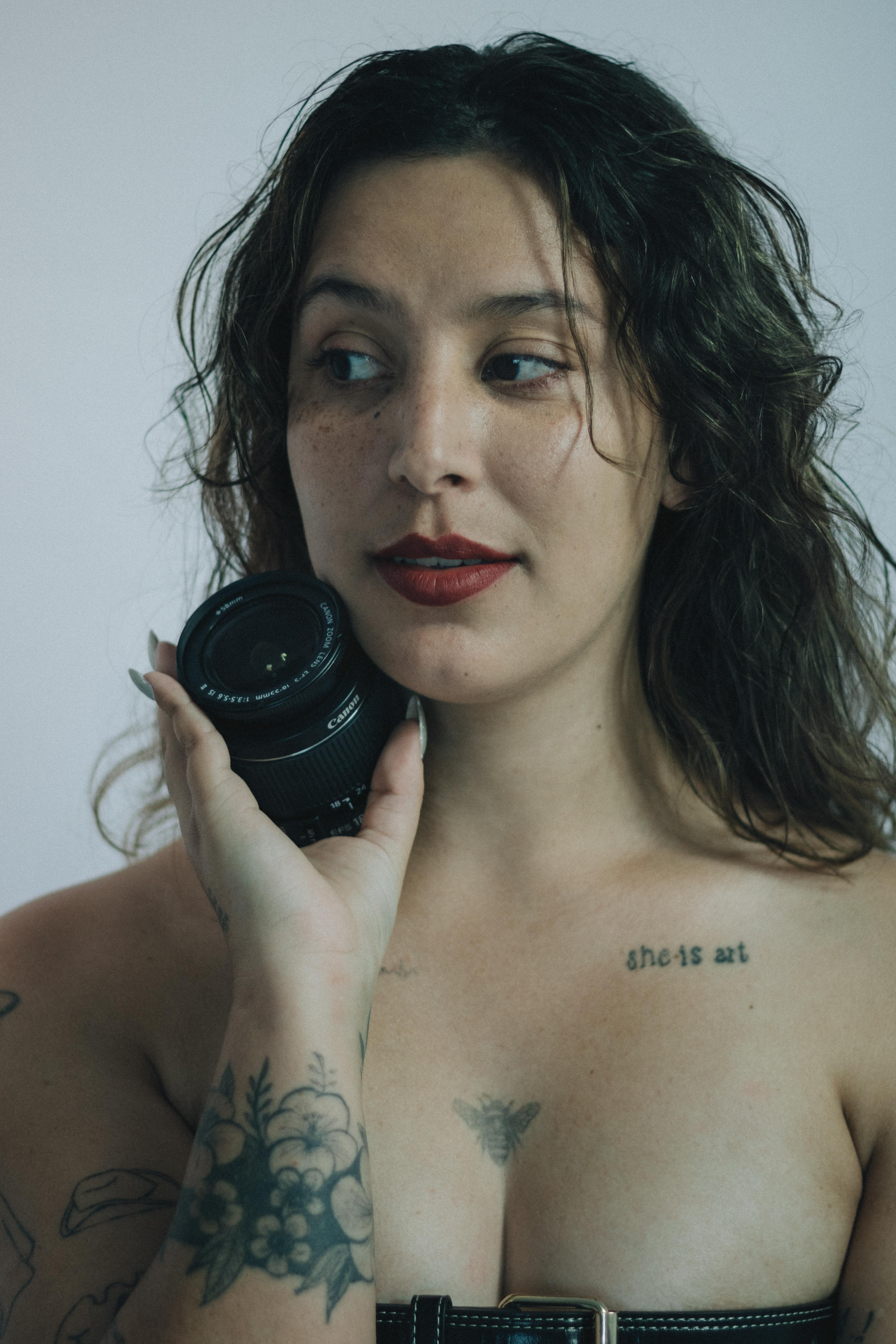 Artistic portrait of a tattooed woman holding a camera lens, evoking creativity and self-expression.