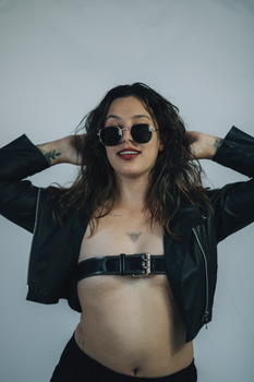 Confident woman in a leather jacket and sunglasses striking a stylish pose indoors.
