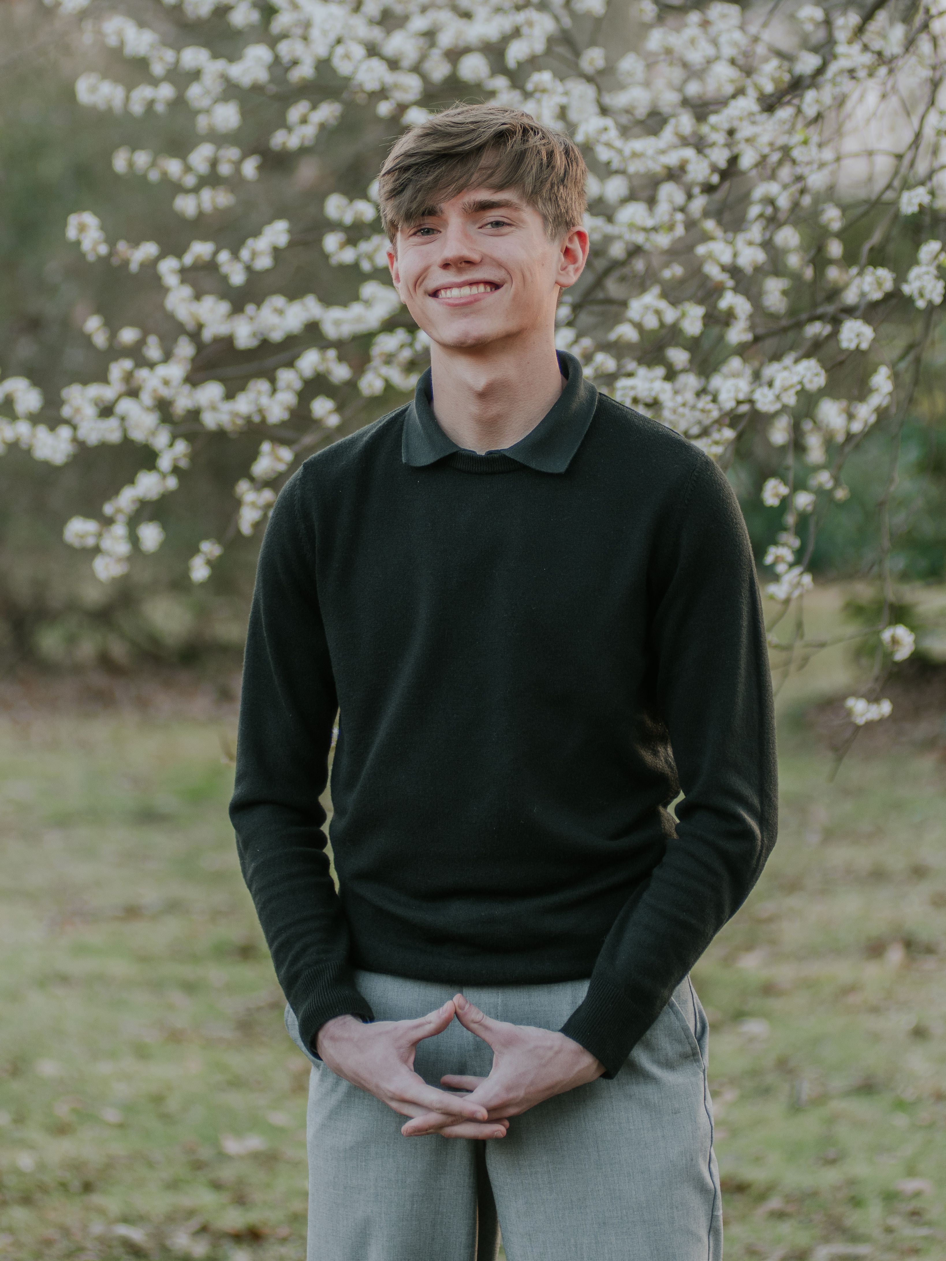 Young man smiling in an outdoor setting with spring blossoms.