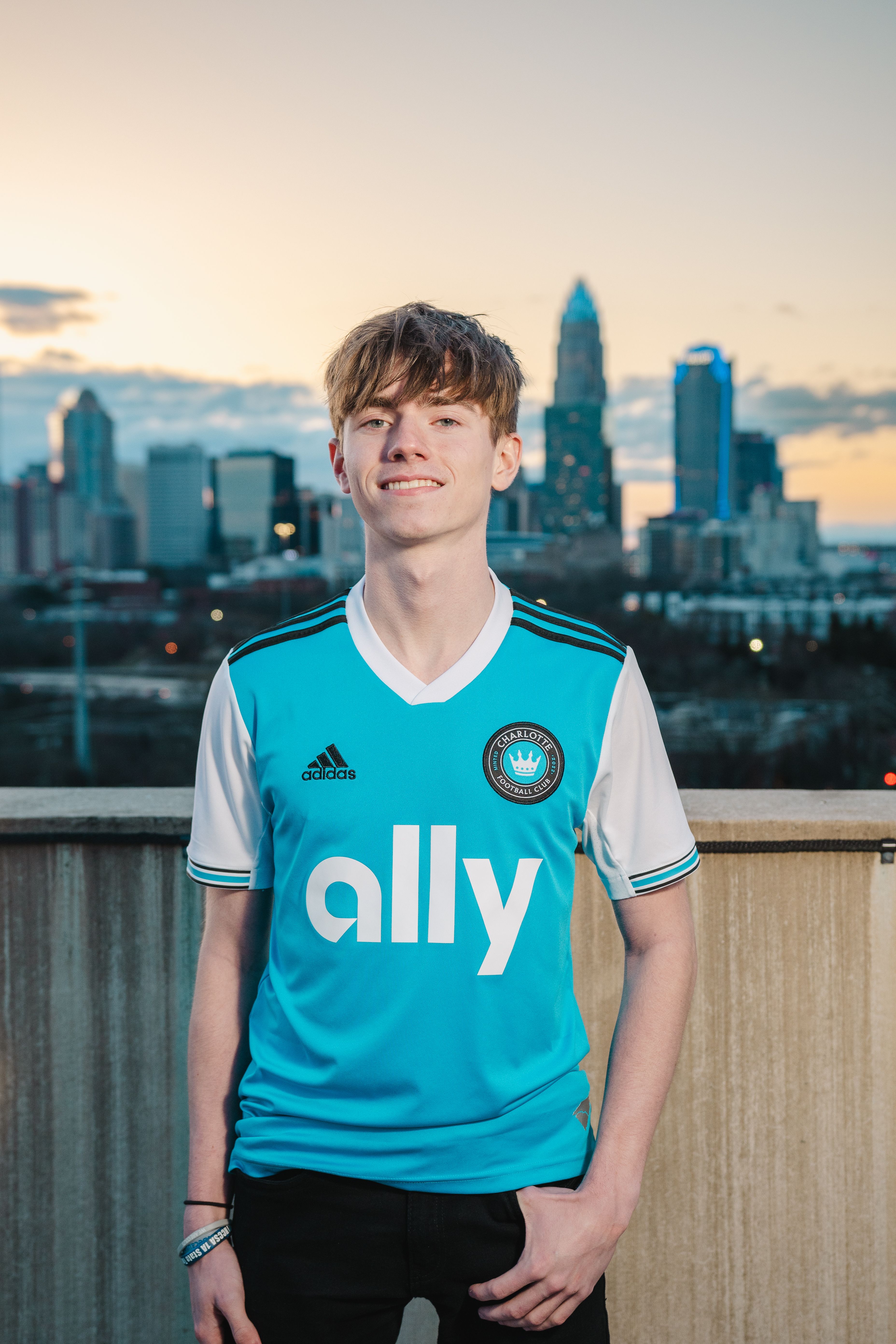 Portrait of a young man in sportswear with a city skyline backdrop at sunset.