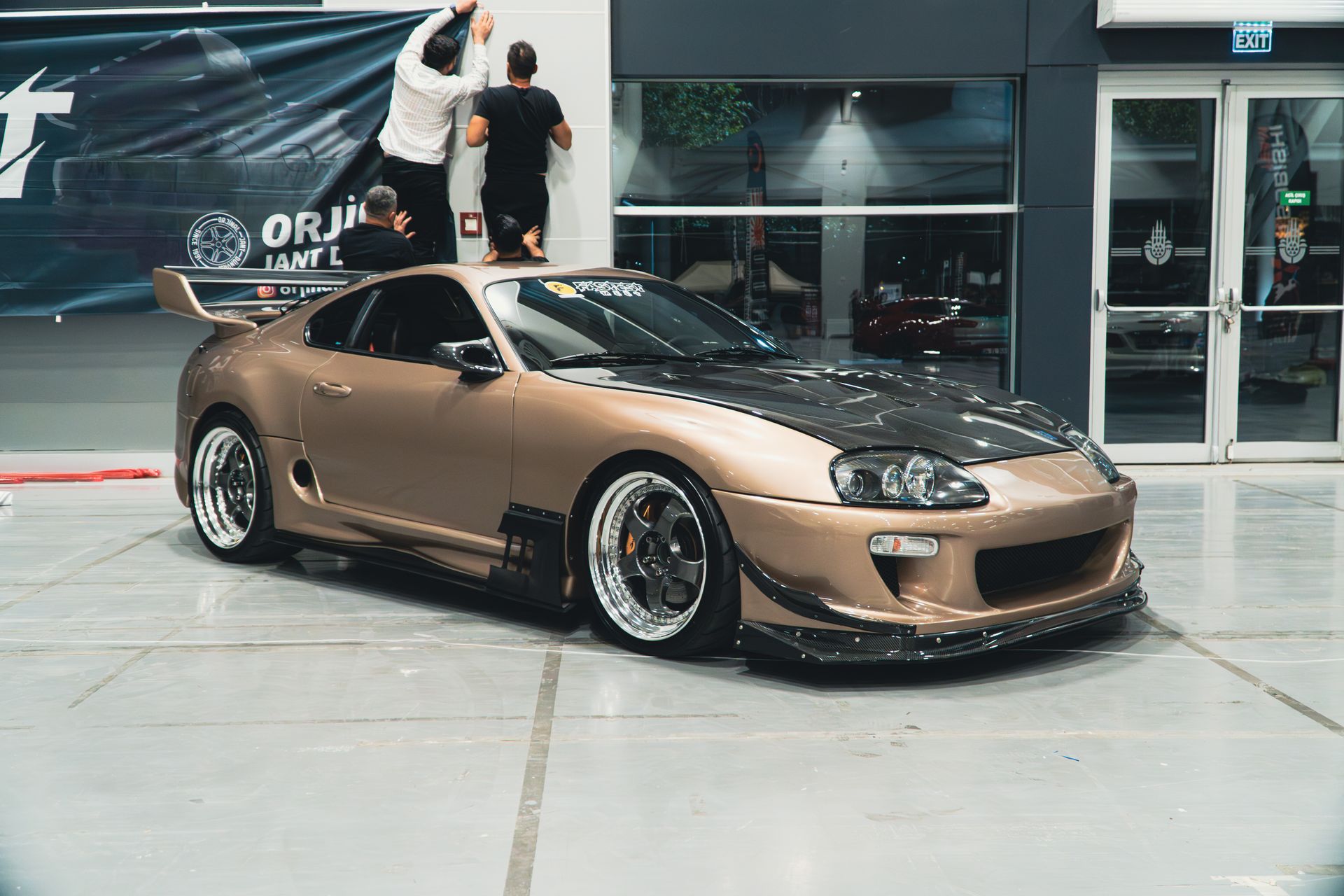 A stylish bronze Toyota Supra showcased indoors at a car event, highlighting its modern design and appeal.