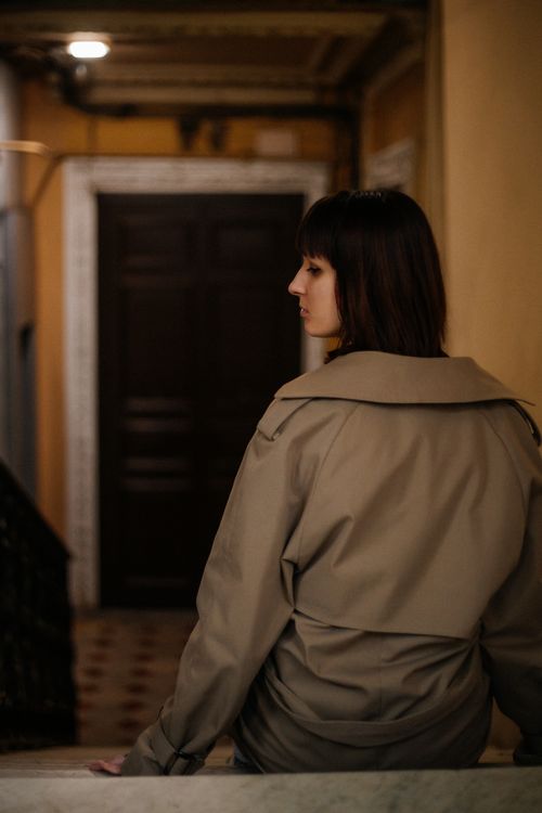 Free Woman in trench coat sitting in dimly lit hallway, thoughtful mood. Stock Photo