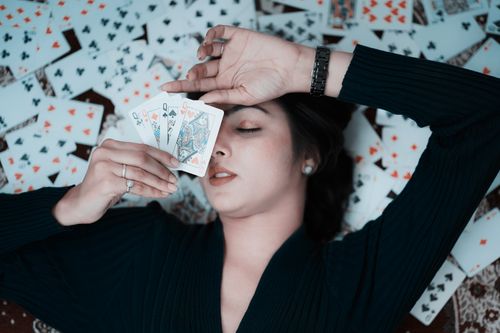 Free Woman lying on playing cards, holding three face cards, creating a creative and stylish scene. Stock Photo