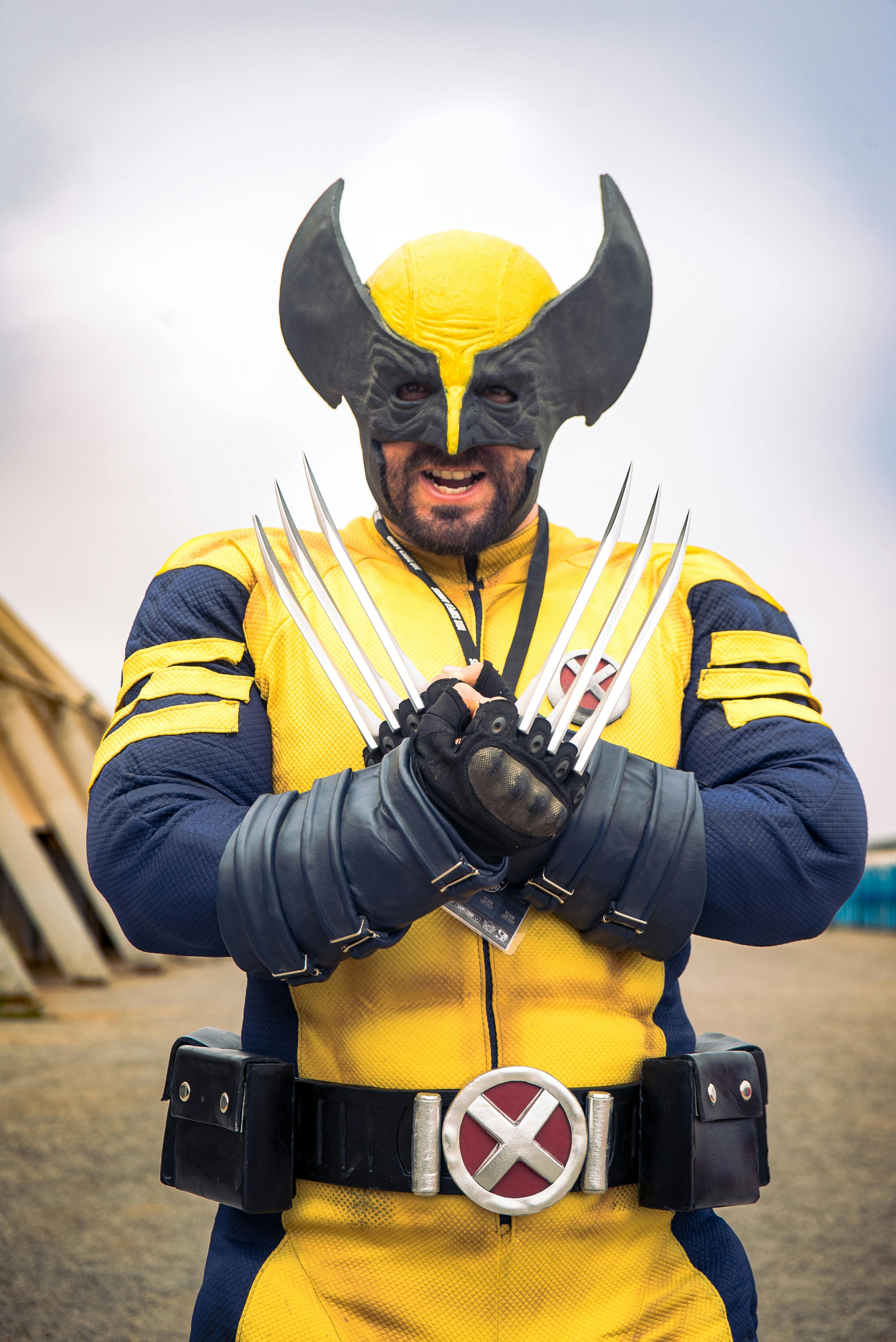An adult in a detailed Wolverine costume poses outdoors with clawed gloves.