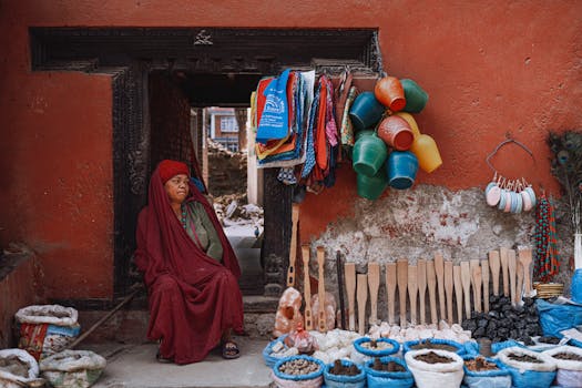 A local woman in red attire at a colorful Kathmandu marketplace, surrounded by goods and textiles.