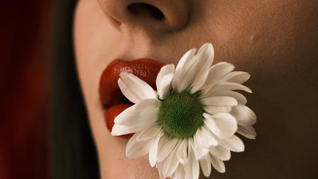 Artistic close-up image of red lips holding a white daisy flower.