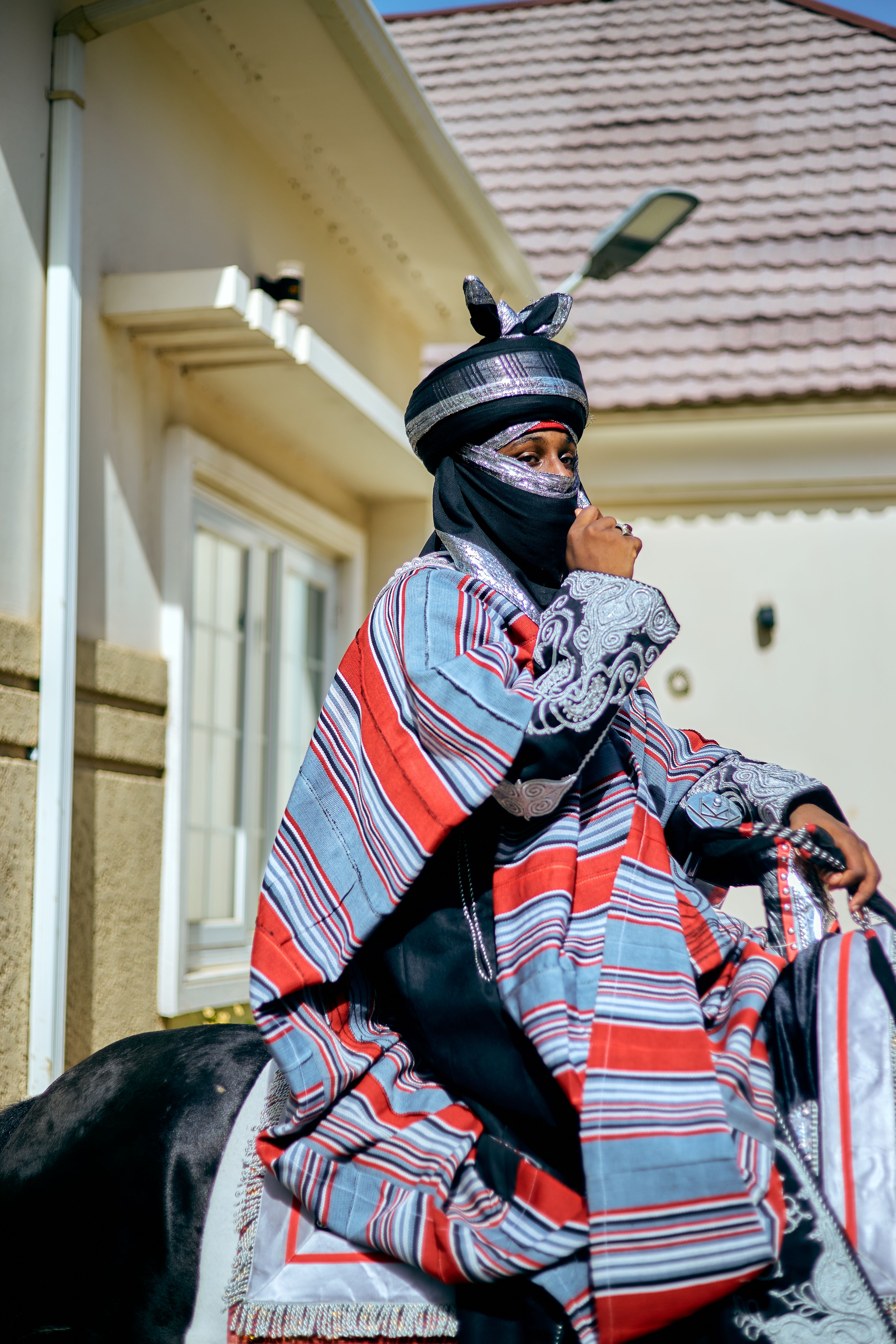 Man in vibrant traditional attire on horseback outside a building.