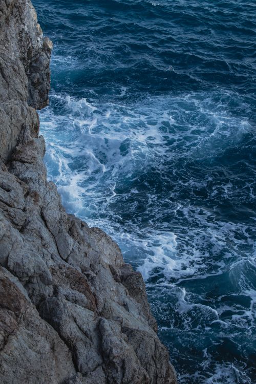Free A rugged cliff edge meets the vibrant blue ocean waves below, capturing a natural seascape. Stock Photo
