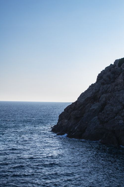 Free A tranquil view of the rocky cliff meeting the vast blue ocean under a clear sky. Stock Photo