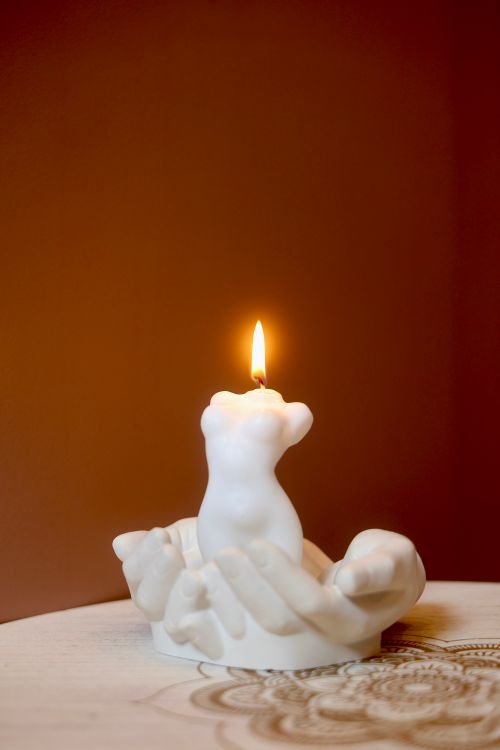 Free White candle shaped like torso held by sculpted hands on wooden surface, warm ambiance. Stock Photo
