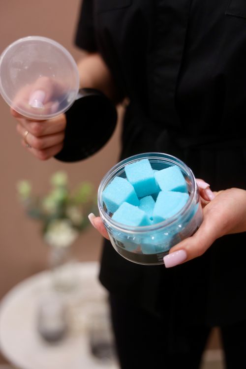 Free Person holding a jar of vibrant blue sugar cubes with a lid, seen indoors. Stock Photo