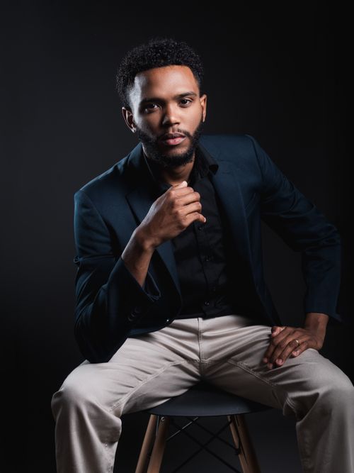 Free Elegantly dressed young man posing confidently on a stool against a dark background. Stock Photo