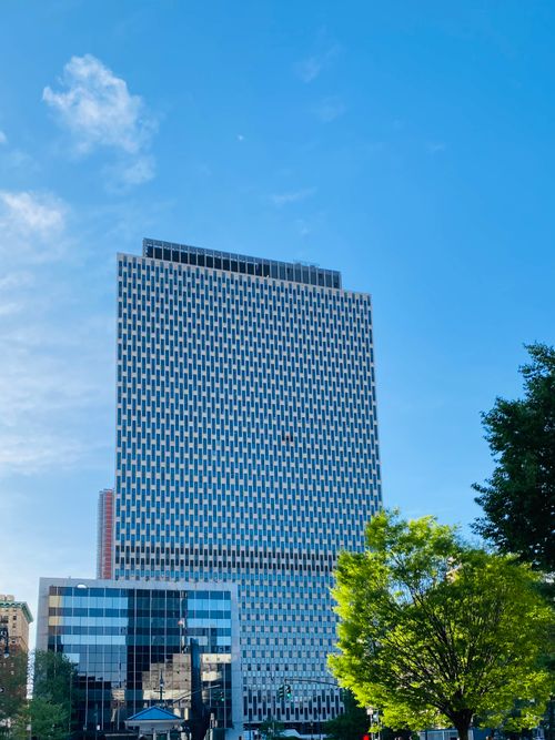 Free Tall modern skyscraper in New York City with blue sky and lush green trees. Stock Photo