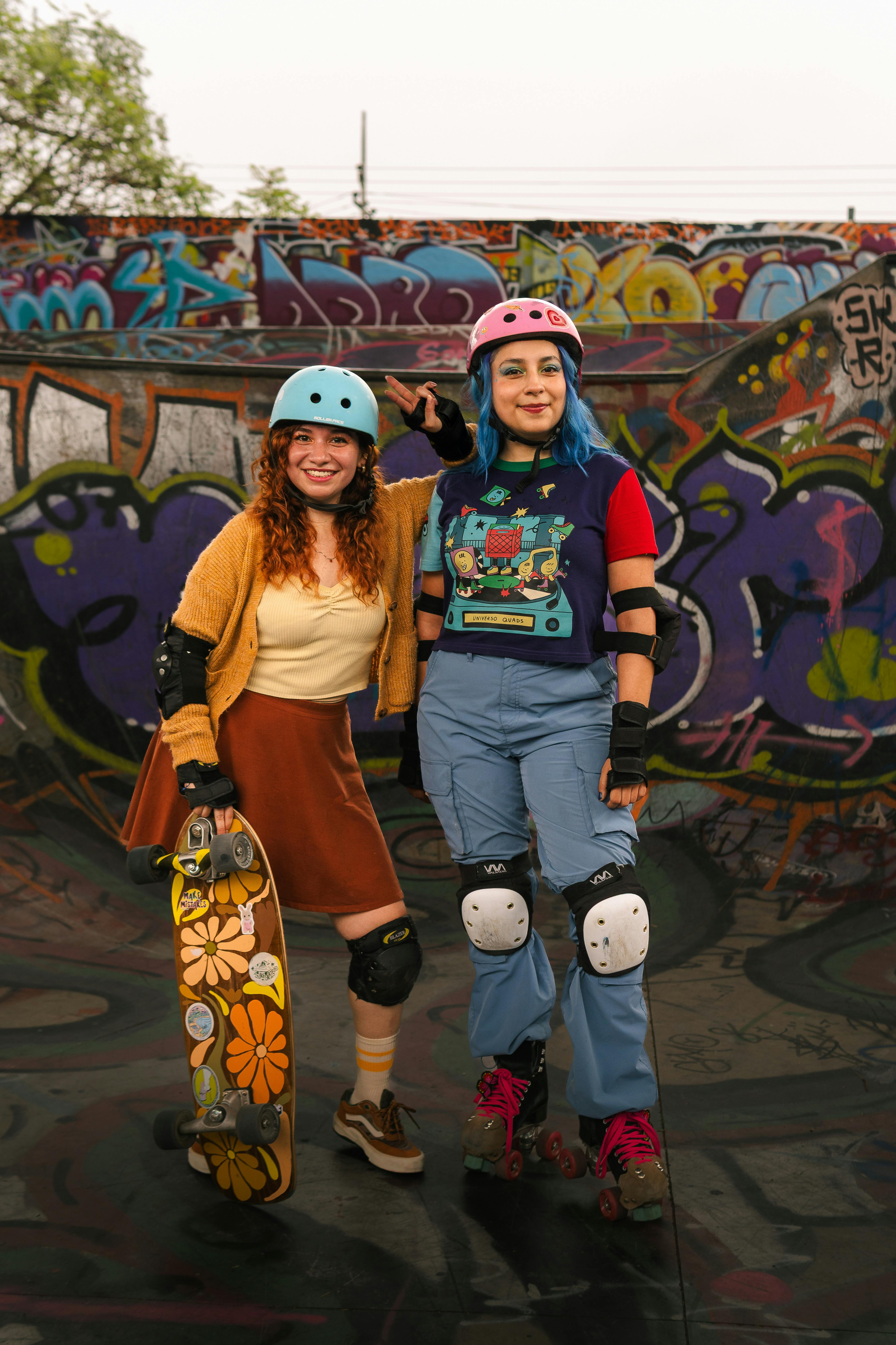 Two female skaters stand at a graffiti-covered skatepark, embracing skate culture.