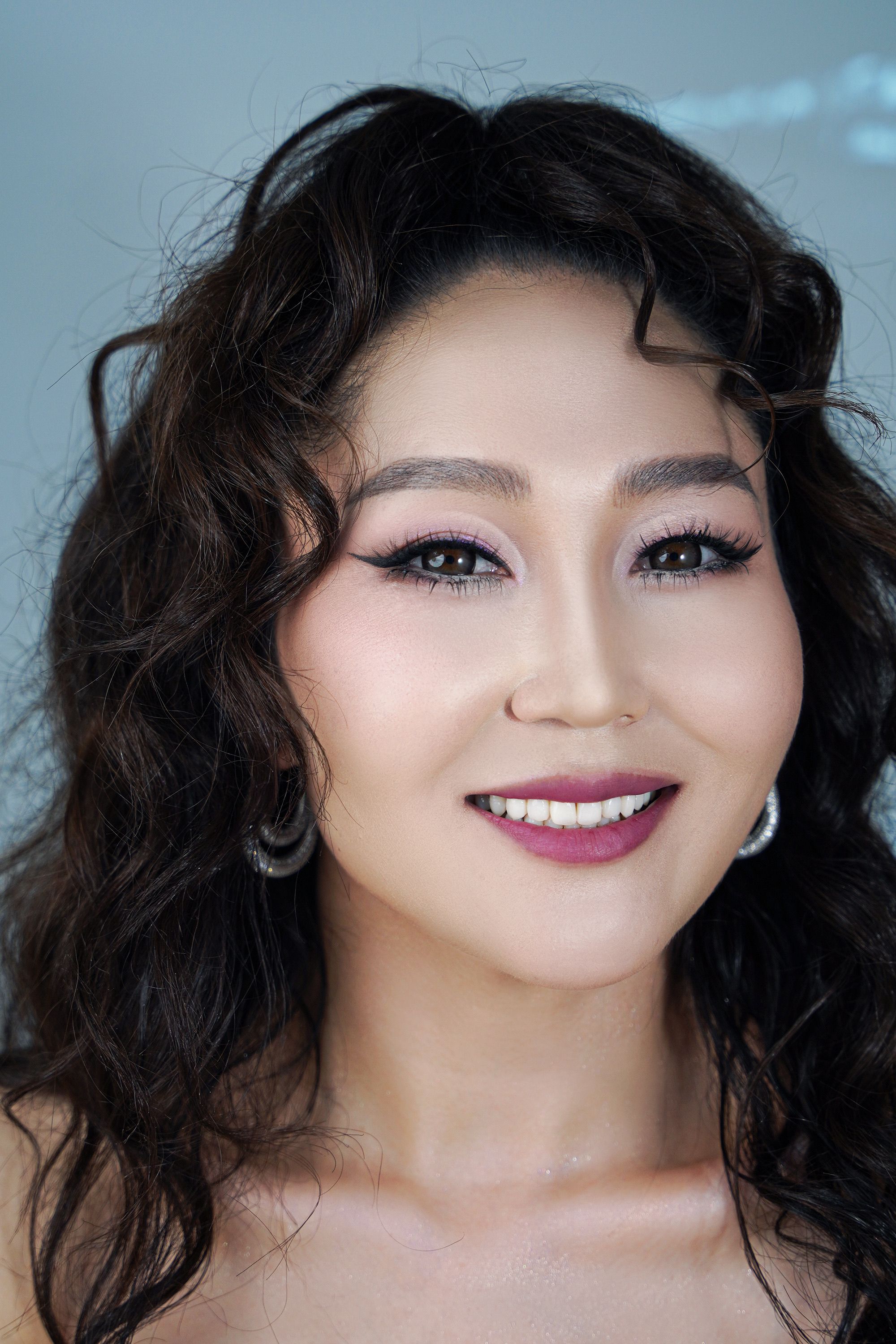 Close-up portrait of a woman with curly hair and elegant makeup, exuding confidence.